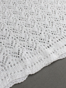 Detailed close-up of white crochet knit fabric with intricate hollow lace patterns