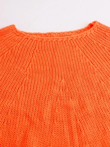 Detailed view of the bright orange knit sweater's ribbed neckline and decorative stitching