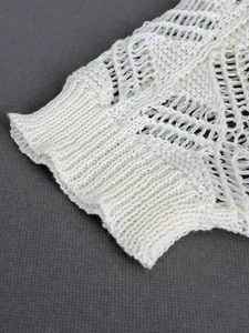 Detail of white crochet knit cardigan featuring hollow diamond patterns and ribbed cuffs