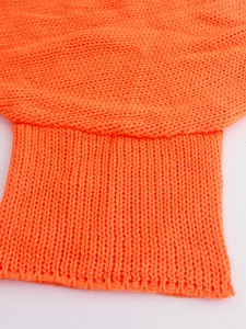 Detailed macro view of orange knit sweater showing ribbed cuffs and premium textured fabric