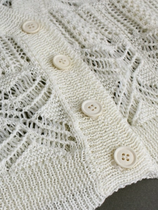 Close-up of knit hollow short cardigan with white round buttons and intricate crochet patterns