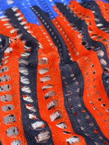 Close-up of hollowed-out knit texture with orange, black, and blue stripes