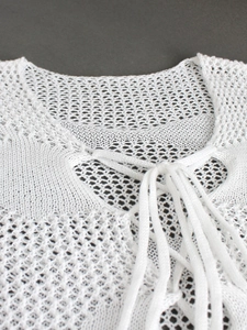 Macro shot of the V-neck lace-up detail on this white crochet hollow-out knit dress
