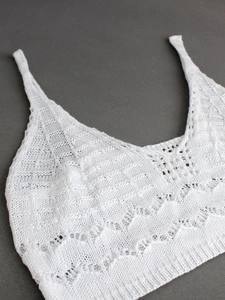 Detailed macro view of white knit camisole top featuring intricate hollow wavy patterns