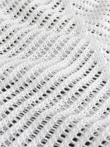 Close-up of white knitted fabric with wave-like hollow pattern for summer beachwear