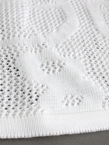 Close-up of white knitted fabric with intricate hollow-out weave pattern for beach dress