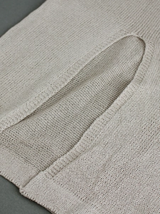 Detailed close-up of light beige knit fabric showing fine stitching and seamless pocket edge