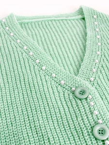 Détail d'un cardigan en maille vert clair avec perles blanches décoratives et boutons assortis