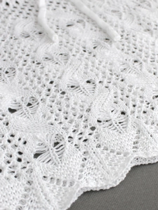 Macro view of white crochet knit fabric with delicate hollow patterns and scalloped edges