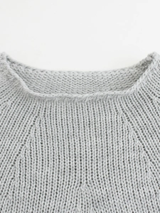 Detail of light grey knit sweater showing round neckline and raglan sleeve texture
