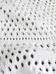 Close-up of white knit crochet fabric with diamond hollow pattern for beach wear