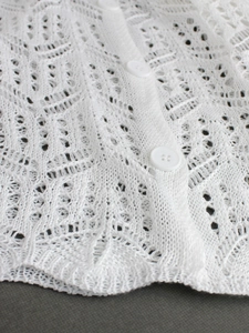 Gros plan détaillé du cardigan en tricot blanc avec motif ajouré et boutons ronds