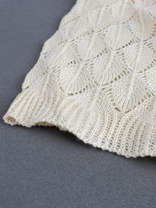 Macro detail of cream knit cardigan featuring leaf pattern texture and ribbed hem edge