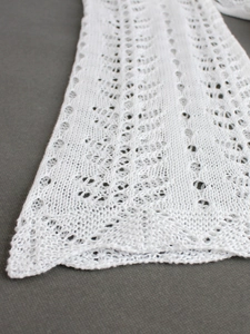 Detailed close-up of white pointelle knit fabric with delicate hollow patterns and fine texture