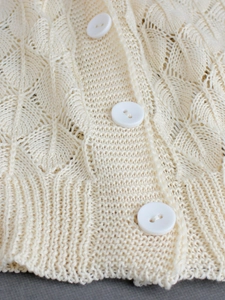 Detail of cream V-neck knit cardigan with leaf hollow pattern and white buttons