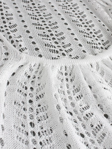 Close-up detail of white wavy hollow knit pattern and scalloped neckline on beach dress