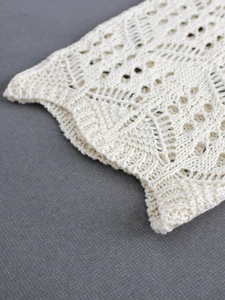 Détail macro du cardigan en tricot crème avec motif complexe de crochet ajouré et texture