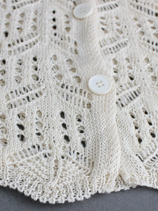 Gros plan du cardigan en maille ajourée blanc crème avec motifs crochet et boutons ronds