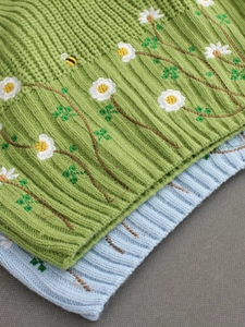 Close-up of green and blue knitted vests with daisy and bee embroidery texture
