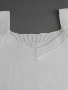 Close-up of white knitted vest showing V-neckline detail and ribbed texture edges