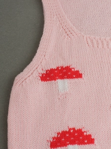 Detail of pink knitted top with red and white mushroom patterns and ribbing