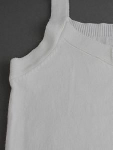 Detail of white knit camisole neckline and strap stitching on a gray background