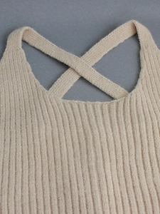 Detail of ribbed knit beige crop top featuring criss-cross strap design and soft texture