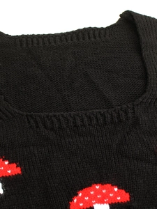Detail of a black knit top with a square neckline and cute red mushroom pattern