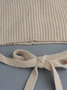 Close-up of beige ribbed knit fabric detail featuring a soft texture and a stylish bow-tie hem