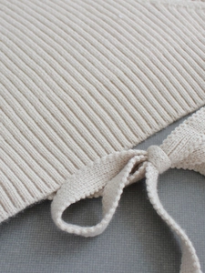 Close-up of cream knit fabric with vertical rib texture and delicate bow tie detail