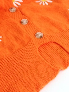 Detailed macro view of orange knit cardigan with white daisy embroidery and marble buttons
