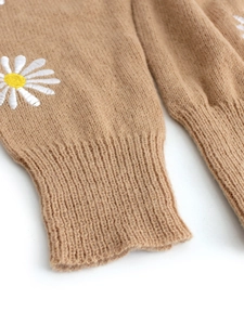 Detailed close-up of brown knit sweater cuff with white daisy embroidery and ribbed texture