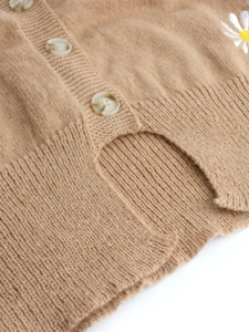 Detailed close-up of brown knit cardigan with daisy embroidery and round cream buttons