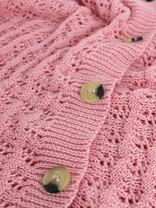 Détail d'un gilet rose en maille ajourée montrant le crochet délicat et le bouton marbré