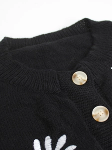 Close-up of black knit cardigan with ribbed crew neck and marble pattern buttons