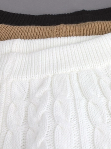 Dettaglio della trama a treccia su capi in maglia nei colori nero, cammello e bianco