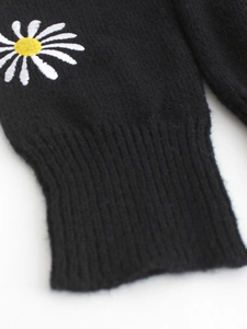 Detail of black knit sleeve cuff with delicate white daisy flower embroidery on fabric