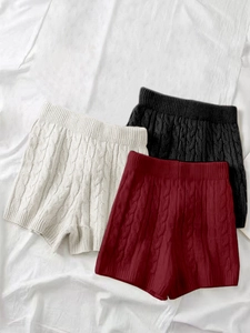 Dettaglio dei pantaloncini in maglia a trecce a vita alta in crema, nero e rosso vino