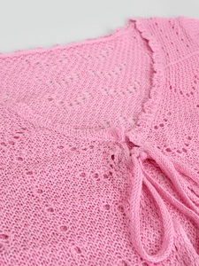 Detalle de top de ganchillo rosa con bordes festoneados y cierre de lazo en el frente