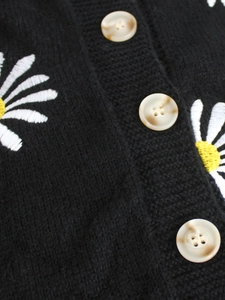 Detailed close-up of white daisy embroidery and amber buttons on black knit cardigan