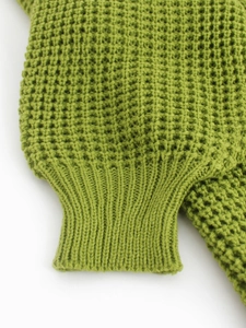 Detail of avocado green waffle knit sweater with thick ribbed cuffs on a white background