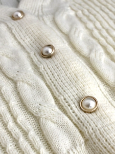 Detail of cable knit pattern and elegant pearl buttons with gold rims on a cardigan