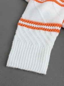 Close-up of white knitted cardigan cuff with orange stripes and delicate openwork texture