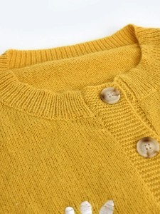 Close-up of bright yellow knit cardigan with round neck, marble buttons and white embroidery
