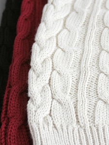 Dettaglio della spessa maglia a trecce e bordo a coste nei colori bianco bordò e nero