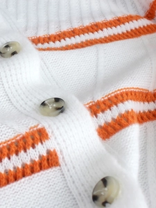 Close-up of white knitted cardigan featuring orange stripes and tortoiseshell buttons