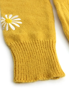 Detail of yellow knit cardigan sleeve with white daisy embroidery and ribbed cuffs