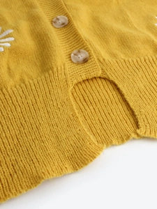 Detail of yellow knit cardigan with white floral embroidery and textured buttons