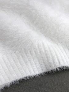 Close-up of white fluffy knit fabric showing soft plush texture and ribbed hem detail