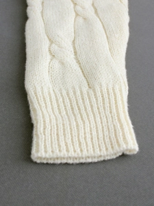 Close-up of cable knit patterns and ribbed cuffs on off-white long sleeve knit dress